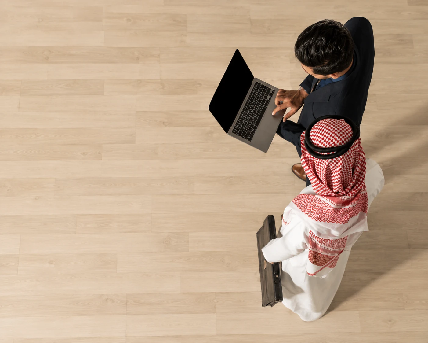 Overhead view of two Saudi professionals discussing analysis over a laptop
